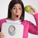 Mujer obesa en dieta sujetando una balanza y una manzana.