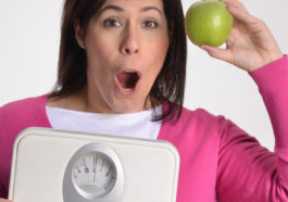 Mujer obesa en dieta sujetando una balanza y una manzana.