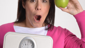 Mujer obesa en dieta sujetando una balanza y una manzana.