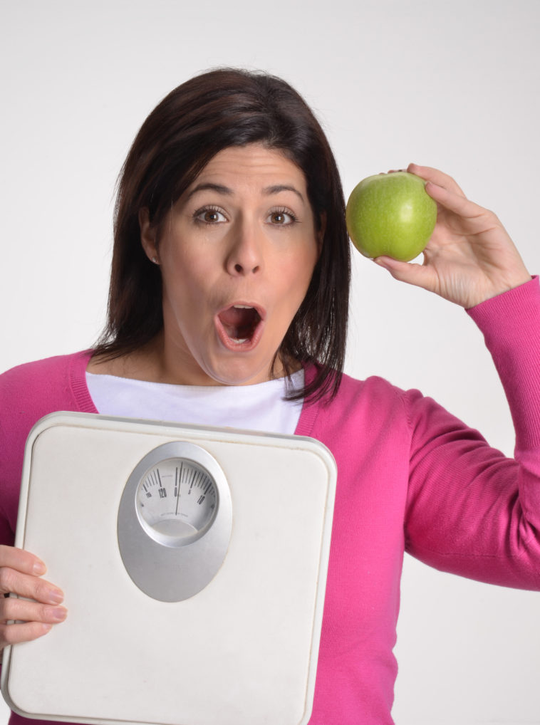 Mujer obesa en dieta sujetando una balanza y una manzana.